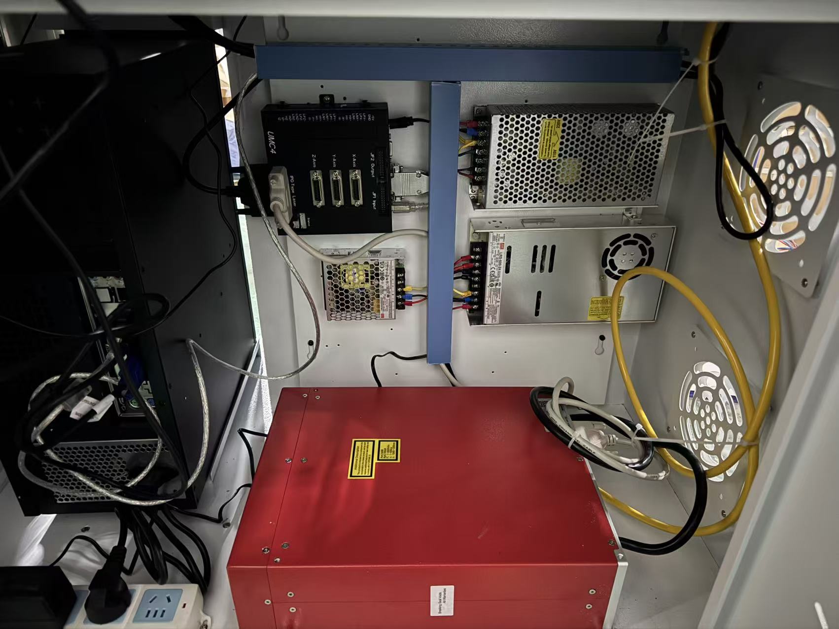 Inside a metal equipment cabinet with a red power unit at the bottom, a metal power supply on the right, and a black controller with multiple ports on the left, with yellow cables nearby