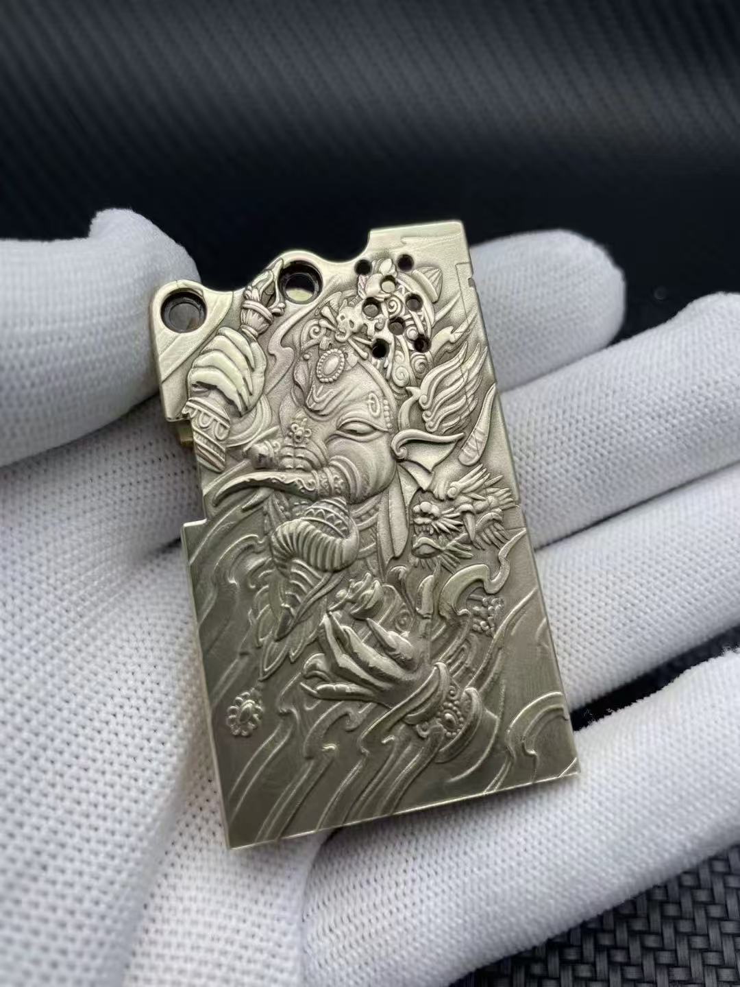 Ornate silver lighter with an embossed Hindu god Ganesha and decorative mythical motifs.